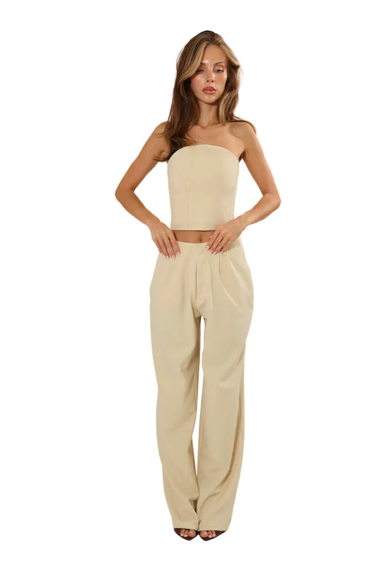 A woman modeling a beige two-piece set consisting of a strapless bandeau crop top and matching high-waisted wide-leg trousers, photographed against a plain white studio background.