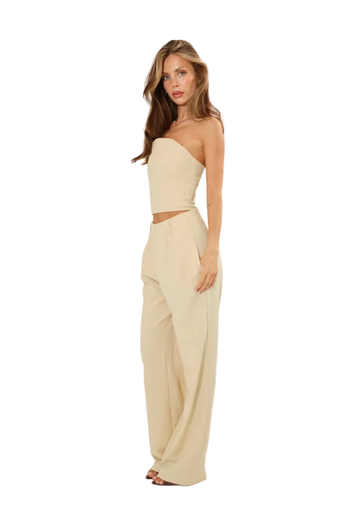 A woman modeling a light beige two-piece set consisting of a strapless crop top and matching wide-leg pants, photographed against a plain white studio background.